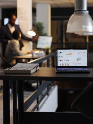 laptop-computer-with-financial-graphs-screen-standing-table-startup-office-coworkers-discussing-company-strategy-background-employees-working-late-night-startup-office-scaled.jpg